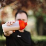 Close-up of a person holding a plastic protein shake tumbler with a red lid outdoors