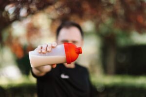 Close-up of a person holding a plastic protein shake tumbler with a red lid outdoors