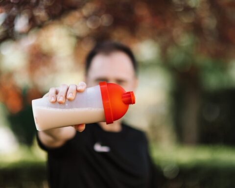 Close-up of a person holding a plastic protein shake tumbler with a red lid outdoors