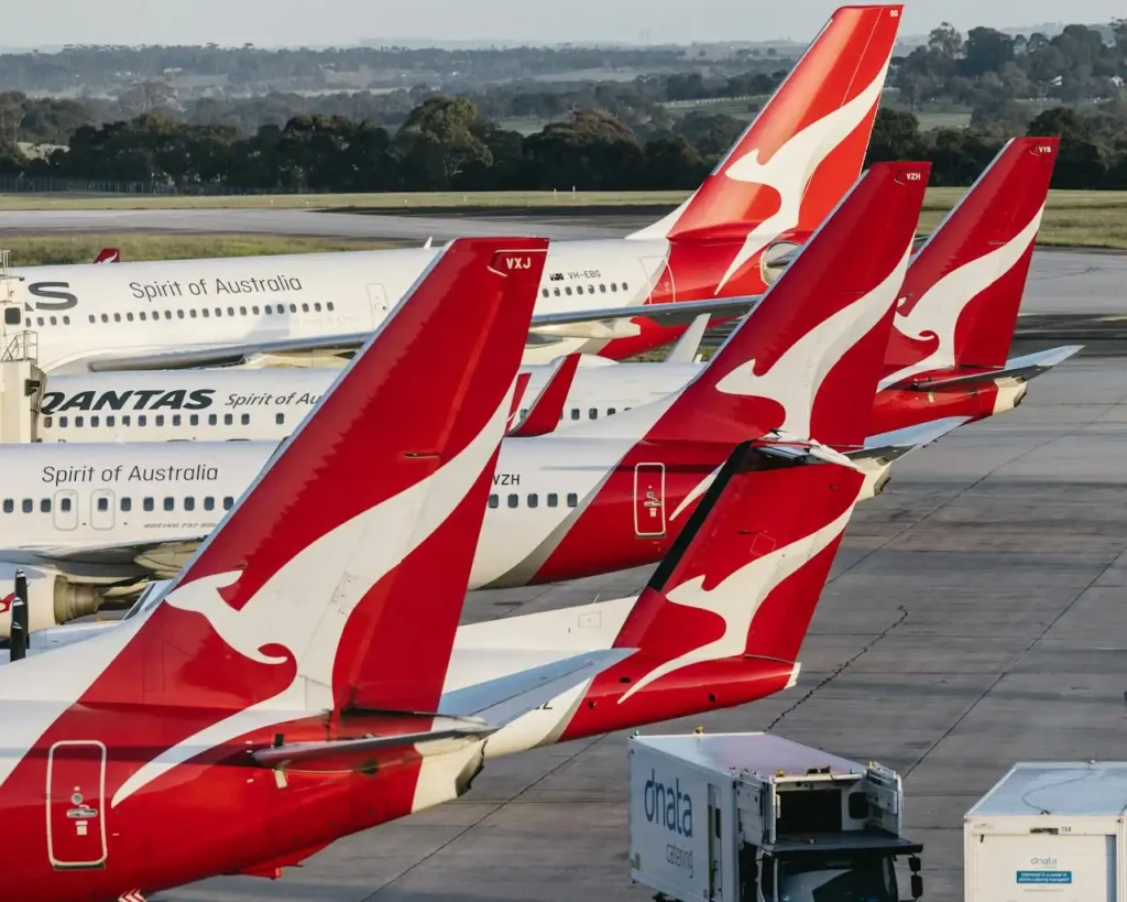 Multiple Qantas aircraft tails at Melbourne Airport with red kangaroo livery, parked on the tarmac in daylight