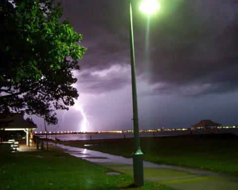View of Brighton towards Redcliffe during a thunderstorm in Queensland, Australia, showing dark storm clouds gathering over the illuminated coastline at night.