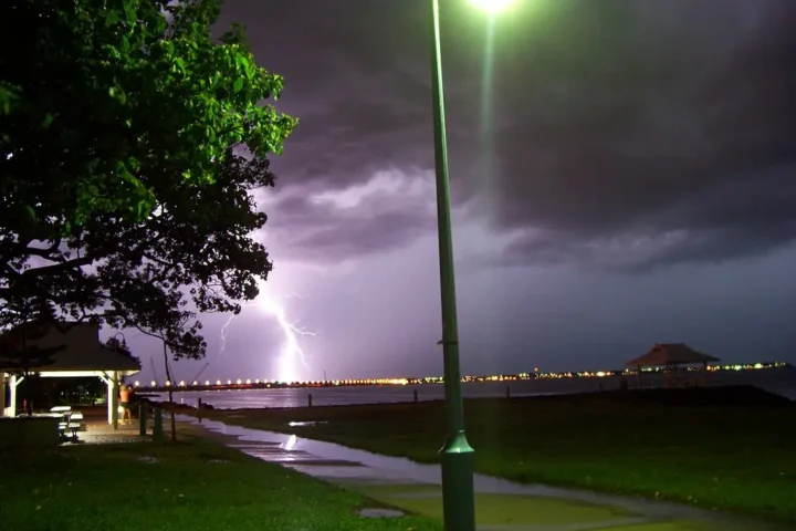 View of Brighton towards Redcliffe during a thunderstorm in Queensland, Australia, showing dark storm clouds gathering over the illuminated coastline at night.