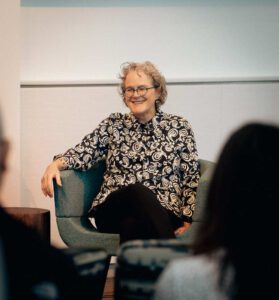 Dr. Jeanne Marrazzo smiling while seated in a blue chair, wearing a black and white patterned blouse during what appears to be an interview or presentation at NIAID.