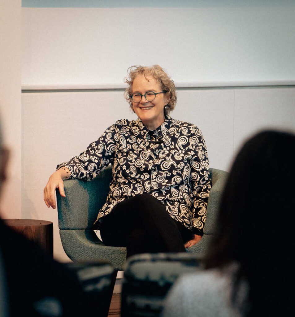 Dr. Jeanne Marrazzo smiling while seated in a blue chair, wearing a black and white patterned blouse during what appears to be an interview or presentation at NIAID.