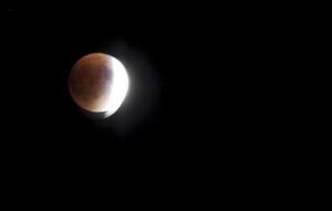 Partial lunar eclipse showing the moon with a reddish glow against a dark background, with part of the moon illuminated and part in shadow.