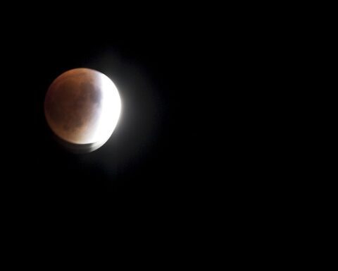 Partial lunar eclipse showing the moon with a reddish glow against a dark background, with part of the moon illuminated and part in shadow.