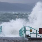 Dark storm clouds looming over a rural landscape with strong winds visibly bending trees
