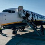 Ryanair Boeing 737 aircraft parked at an airport with passengers boarding via stairs, ground crew visible on tarmac