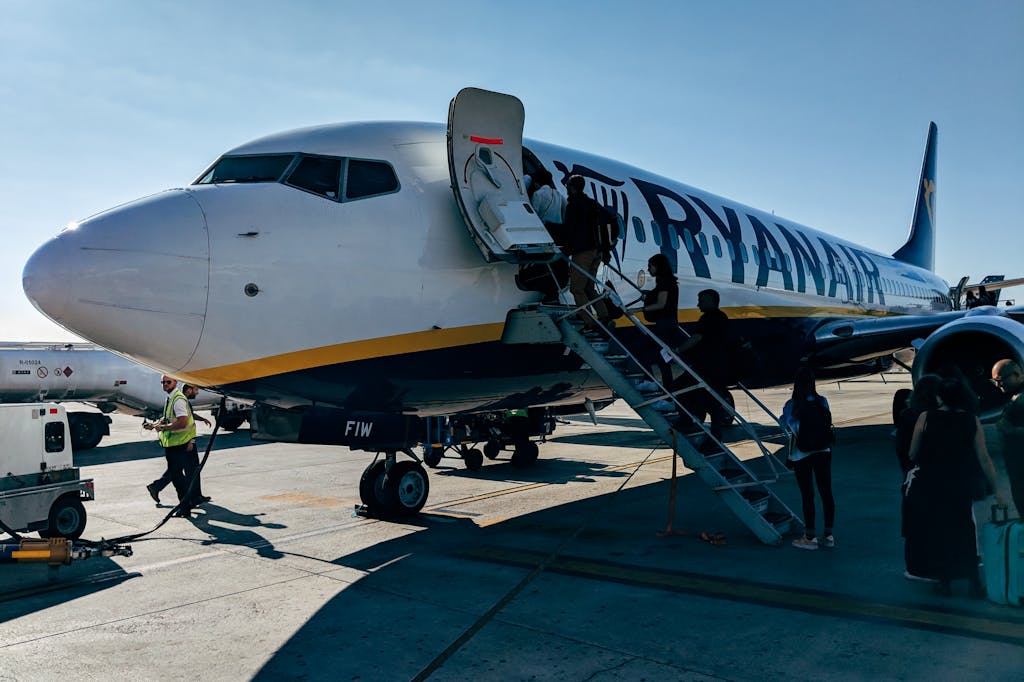 Ryanair Boeing 737 aircraft parked at an airport with passengers boarding via stairs, ground crew visible on tarmac