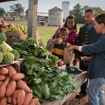 USDA staff member processes a SNAP/EBT transaction at an outdoor farmers’ market stall, helping a shopper use nutrition benefits to buy fresh produce.