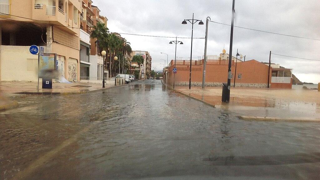 Rain-soaked street in Puerto de Mazarrón, Spain, with reflections on wet pavement and cars parked along the road