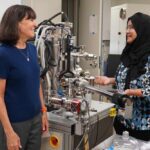 Stacey Bent and Sanzeeda Baig Shuchi standing beside an X-ray photoelectron spectroscopy setup in a Stanford lab.