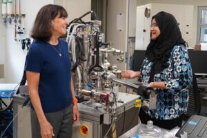 Stacey Bent and Sanzeeda Baig Shuchi standing beside an X-ray photoelectron spectroscopy setup in a Stanford lab.