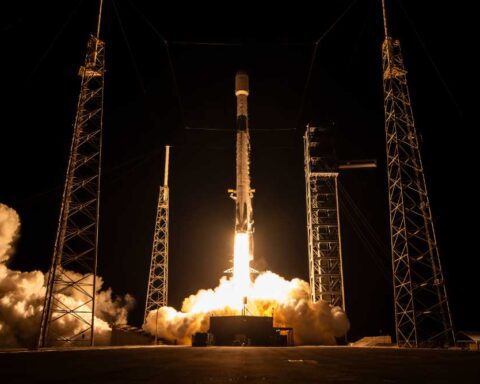 Falcon 9 lifts off at night from SLC-40 for Project Kuiper KF-03, framed by four lightning towers and heavy exhaust plume.