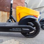 Row of Bird e-scooters lined on a city sidewalk in daylight, buildings in the background.