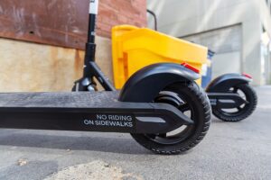 Row of Bird e-scooters lined on a city sidewalk in daylight, buildings in the background.