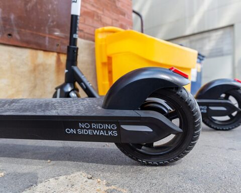 Row of Bird e-scooters lined on a city sidewalk in daylight, buildings in the background.