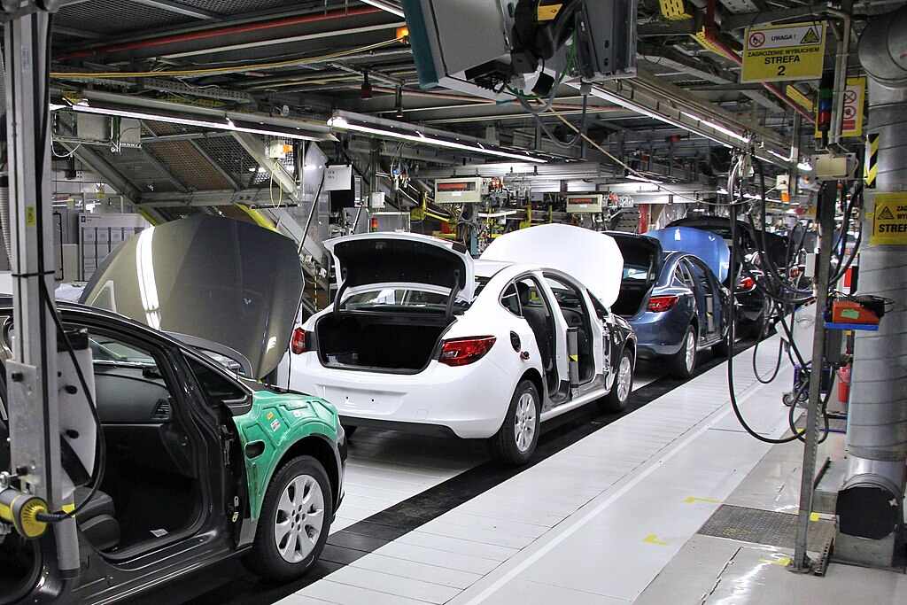 A car factory production line in General Motors Manufacturing Poland, with several car bodies in various stages of assembly.