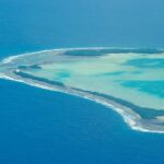 Aerial view of a narrow Tuvalu atoll surrounded by shallow turquoise ocean.