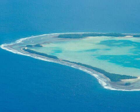 Aerial view of a narrow Tuvalu atoll surrounded by shallow turquoise ocean.