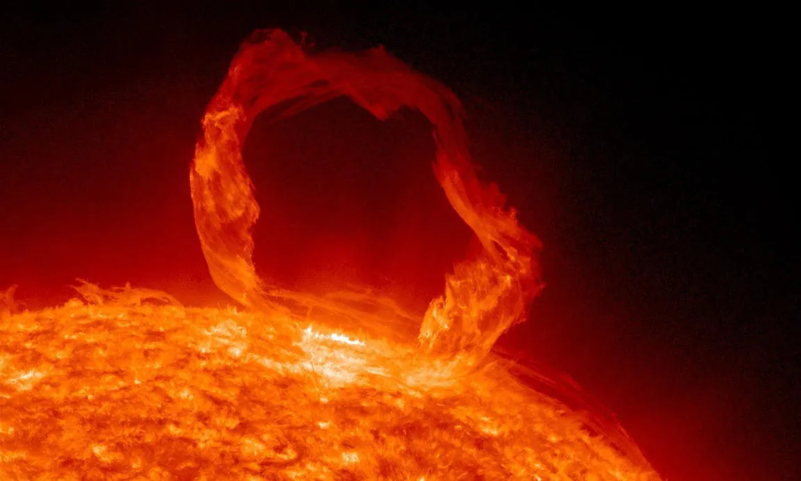 A vibrant red-orange solar flare arc erupting from the sun's surface against the black background of space