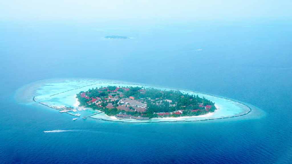 Aerial view of a Maldives resort island with overwater villas and turquoise lagoon