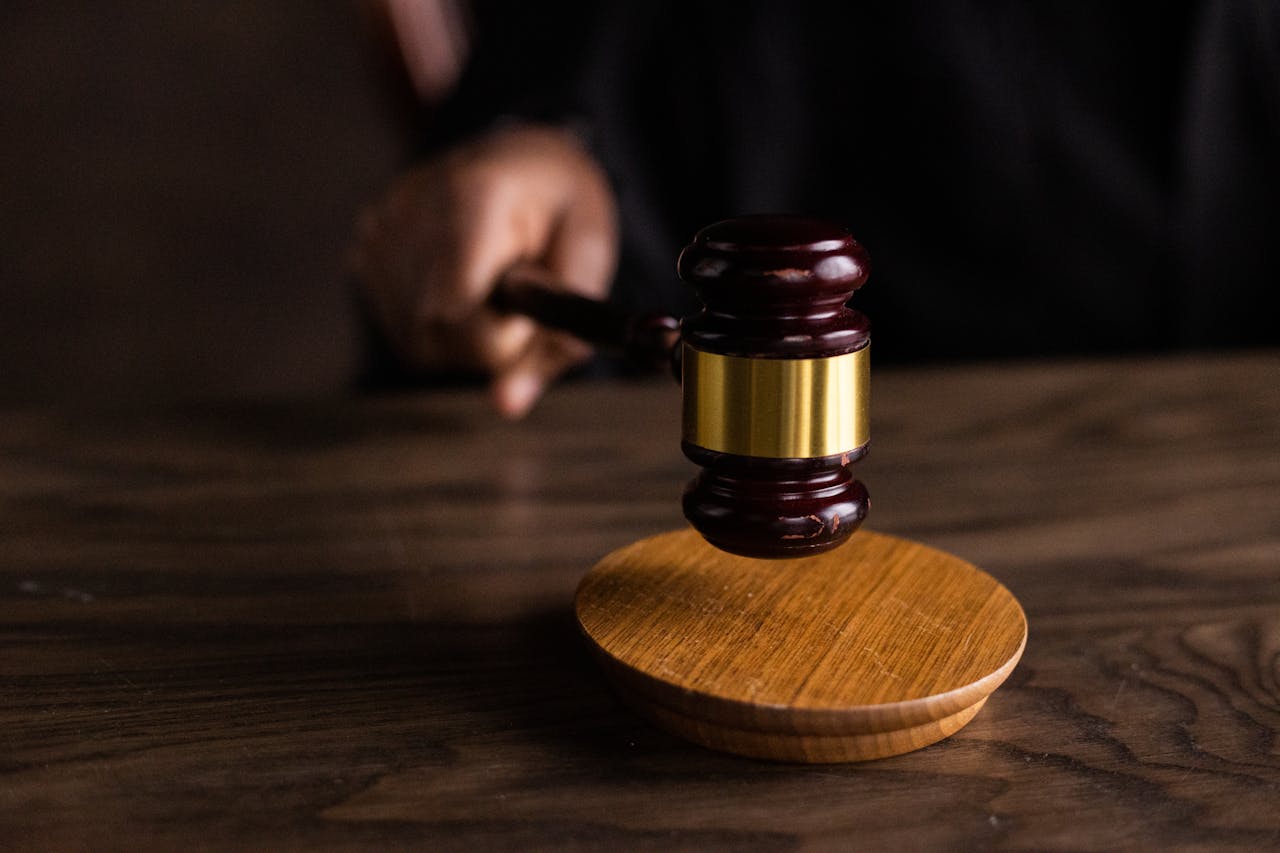 A judge's gavel with wooden base on a dark wooden table with blurred figure in the background, representing legal proceedings and court cases.