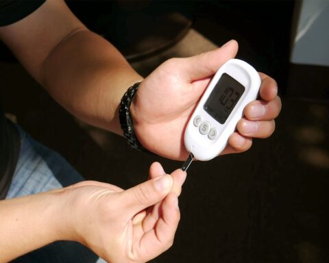 Close-up of hands loading a test strip into a glucometer for a blood sugar check