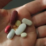 Person holding various supplement pills in the palm of their hand, illustrating the increasing use of synthetic vitamins in daily health routines.