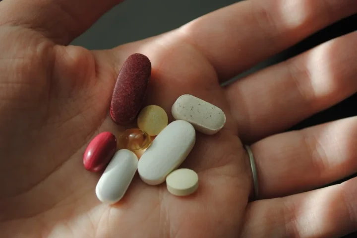 Person holding various supplement pills in the palm of their hand, illustrating the increasing use of synthetic vitamins in daily health routines.