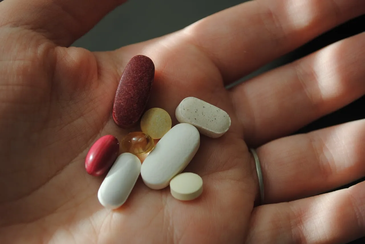 Person holding various supplement pills in the palm of their hand, illustrating the increasing use of synthetic vitamins in daily health routines.