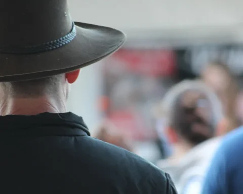 Back view of a person wearing a wide-brimmed Australian outback hat in a public outdoor setting with people in soft focus in the background.