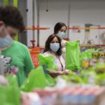 USDA officials touring a food-bank distribution warehouse with volunteers boxing and bagging food items