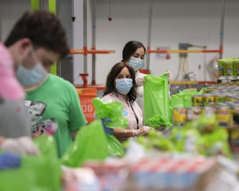 USDA officials touring a food-bank distribution warehouse with volunteers boxing and bagging food items