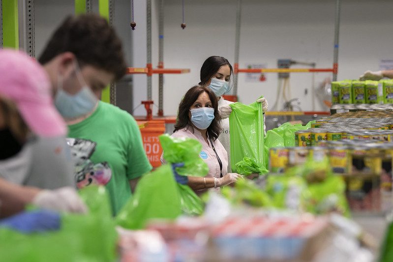 USDA officials touring a food-bank distribution warehouse with volunteers boxing and bagging food items