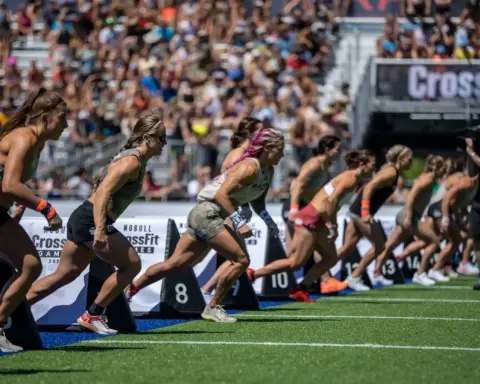 Female athletes sprinting from the start line during a CrossFit Games competition in a packed stadium.