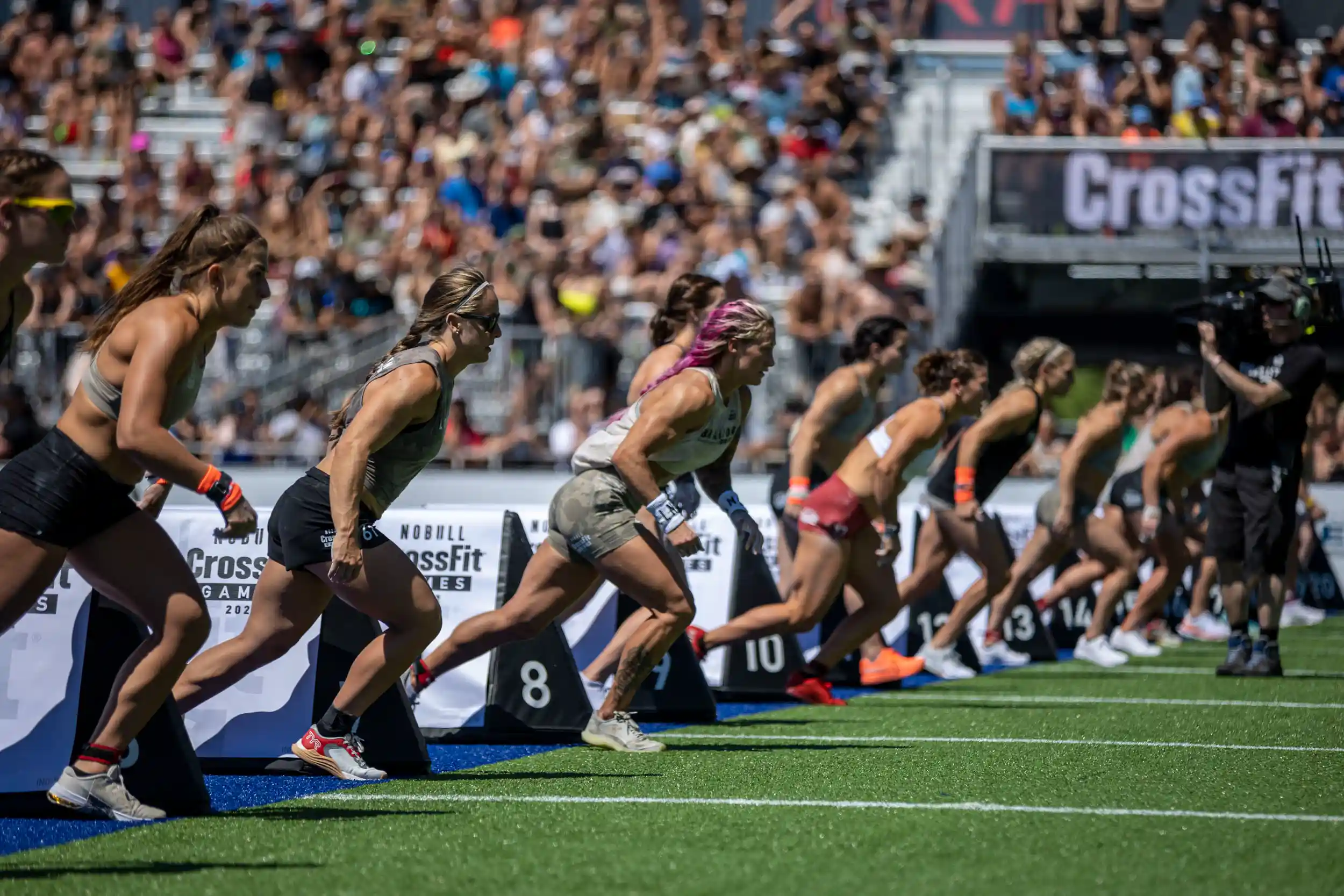 Female athletes sprinting from the start line during a CrossFit Games competition in a packed stadium