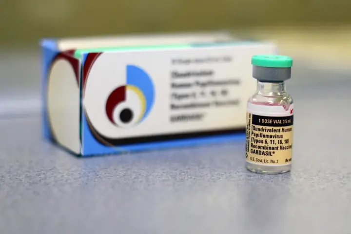 Gardasil HPV vaccine vial placed in front of its packaging box on a clinical surface.