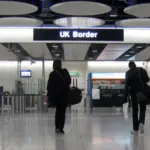 Travellers walking toward UK Border control gates at Heathrow Airport arrivals hall