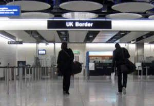 Travellers walking toward UK Border control gates at Heathrow Airport arrivals hall