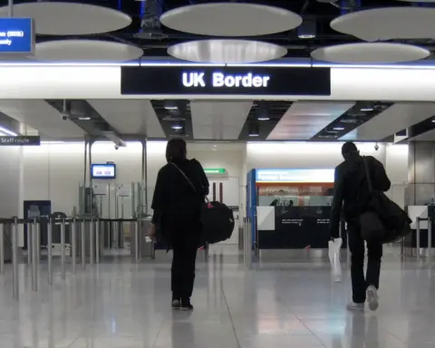 Travellers walking toward UK Border control gates at Heathrow Airport arrivals hall