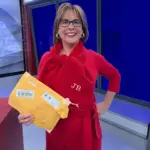 Meteorologist Jeriann Ritter in a red outfit holding a mailed package and wearing a personalized scarf in a TV studio.