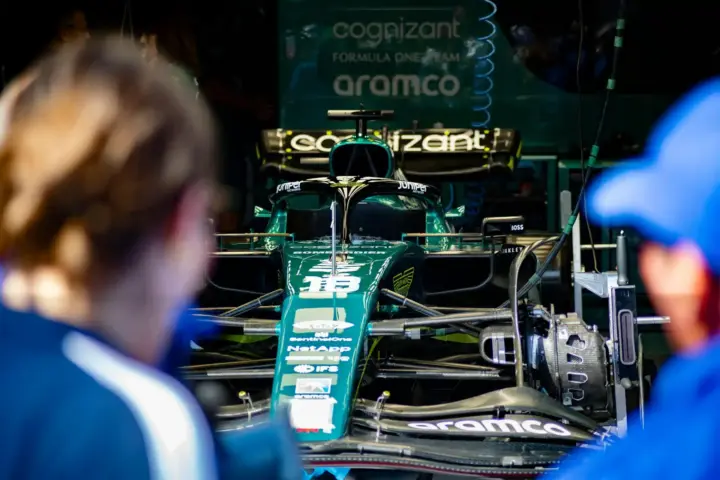 Front view of an Aston Martin Formula 1 car inside the team garage while engineers and team members observe ongoing technical checks.