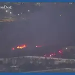 Wildfire burning at night near buildings and roads in San Diego County captured by ALERTCalifornia camera network with emergency vehicles responding