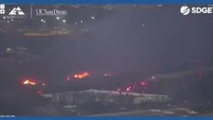 Wildfire burning at night near buildings and roads in San Diego County captured by ALERTCalifornia camera network with emergency vehicles responding