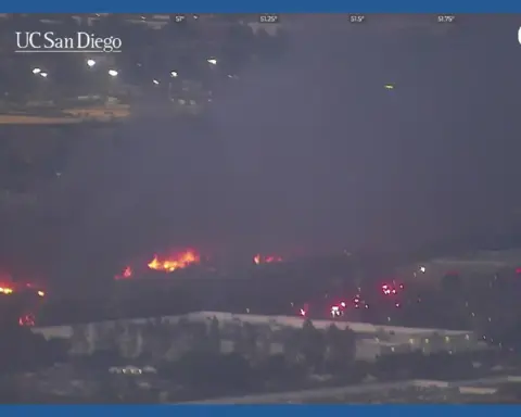 Wildfire burning at night near buildings and roads in San Diego County captured by ALERTCalifornia camera network with emergency vehicles responding