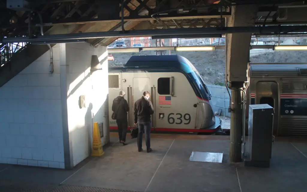 Amtrak passenger train at station platform with two people walking nearby, representing Northeast Corridor rail operations amid MTA access dispute