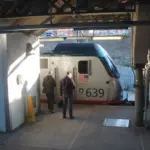Amtrak passenger train at station platform with two people walking nearby, representing Northeast Corridor rail operations amid MTA access dispute