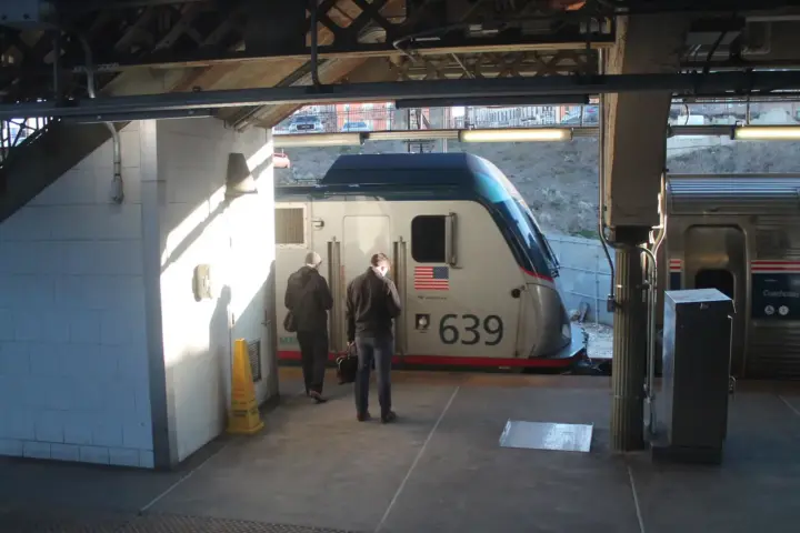 Amtrak passenger train at station platform with two people walking nearby, representing Northeast Corridor rail operations amid MTA access dispute