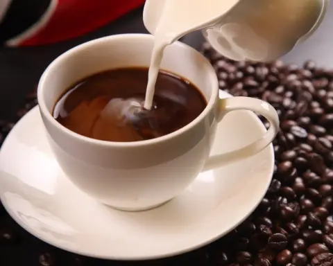 Coffee with milk being poured into a cup with roasted coffee beans, representing daily coffee consumption and its link to gut microbiome and cognitive effects